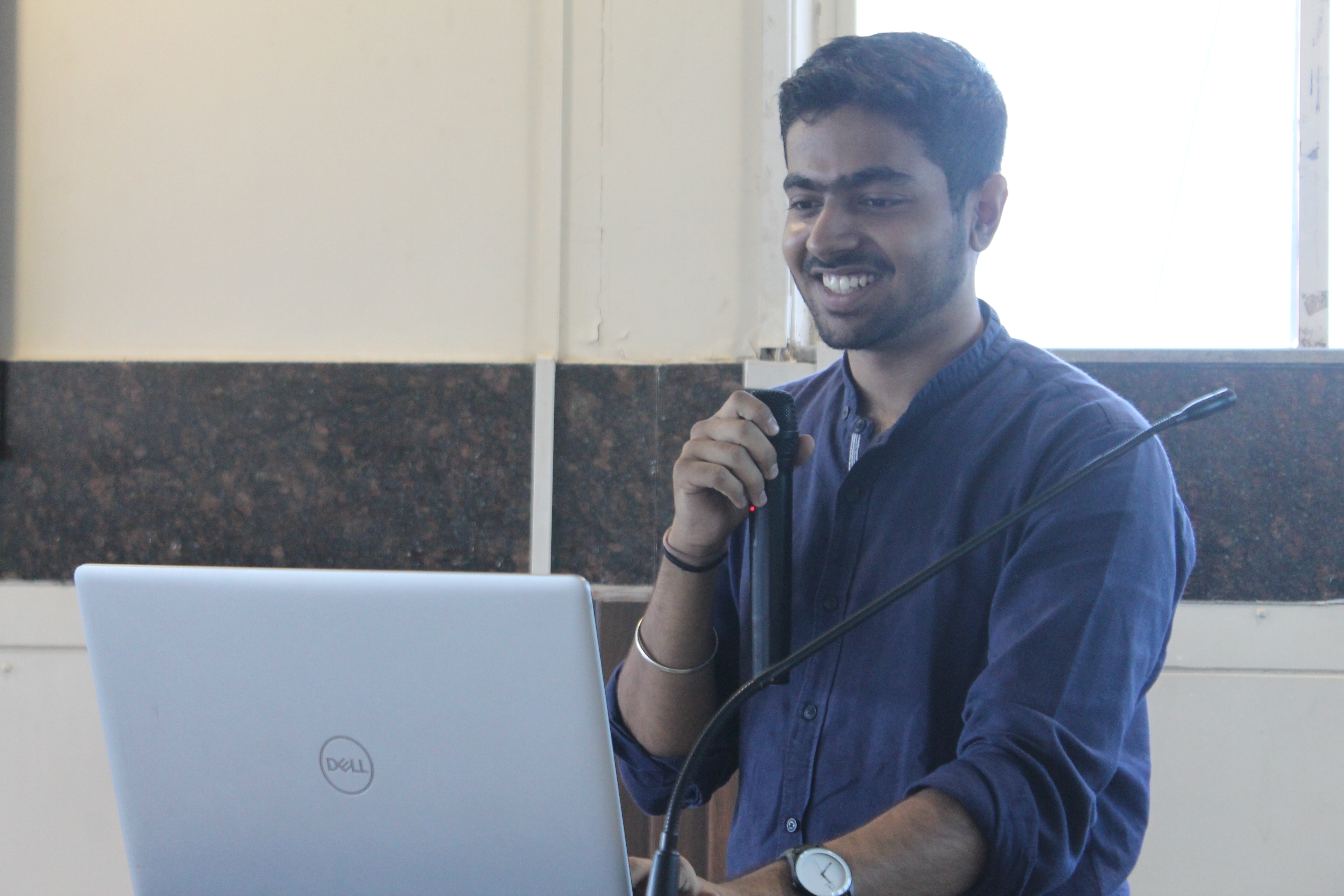 A picture of Tushar Nankani holding a mic on a podium behind a laptop.