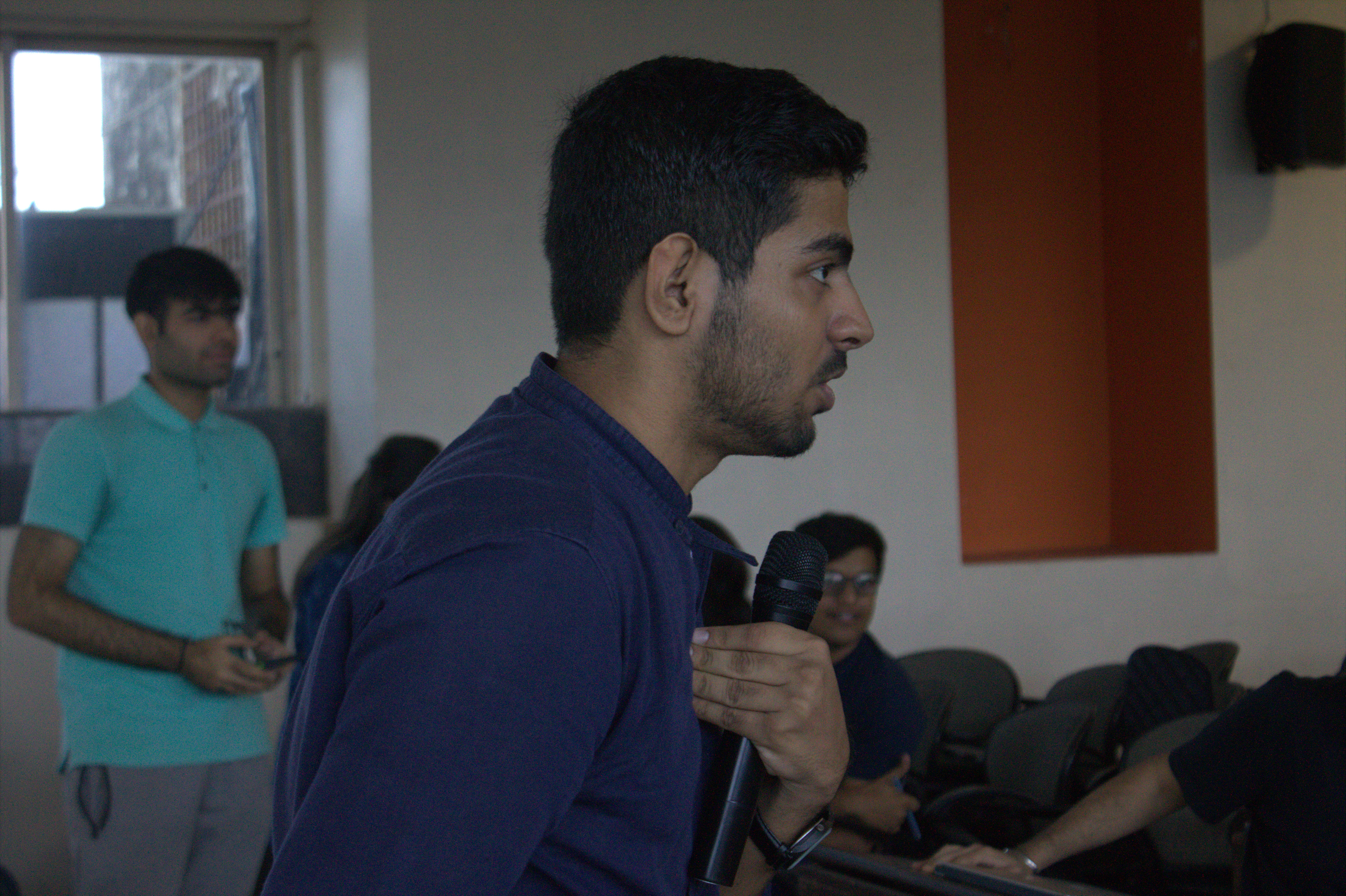 A side-profile picture of Tushar holding a mic and pointing fingers to his chest.